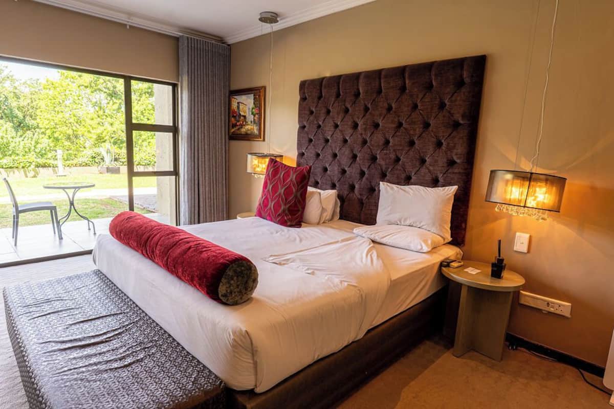 Een hotelkamer met een groot bed, een tafeltje, een lamp en uitzicht op de omgeving.
