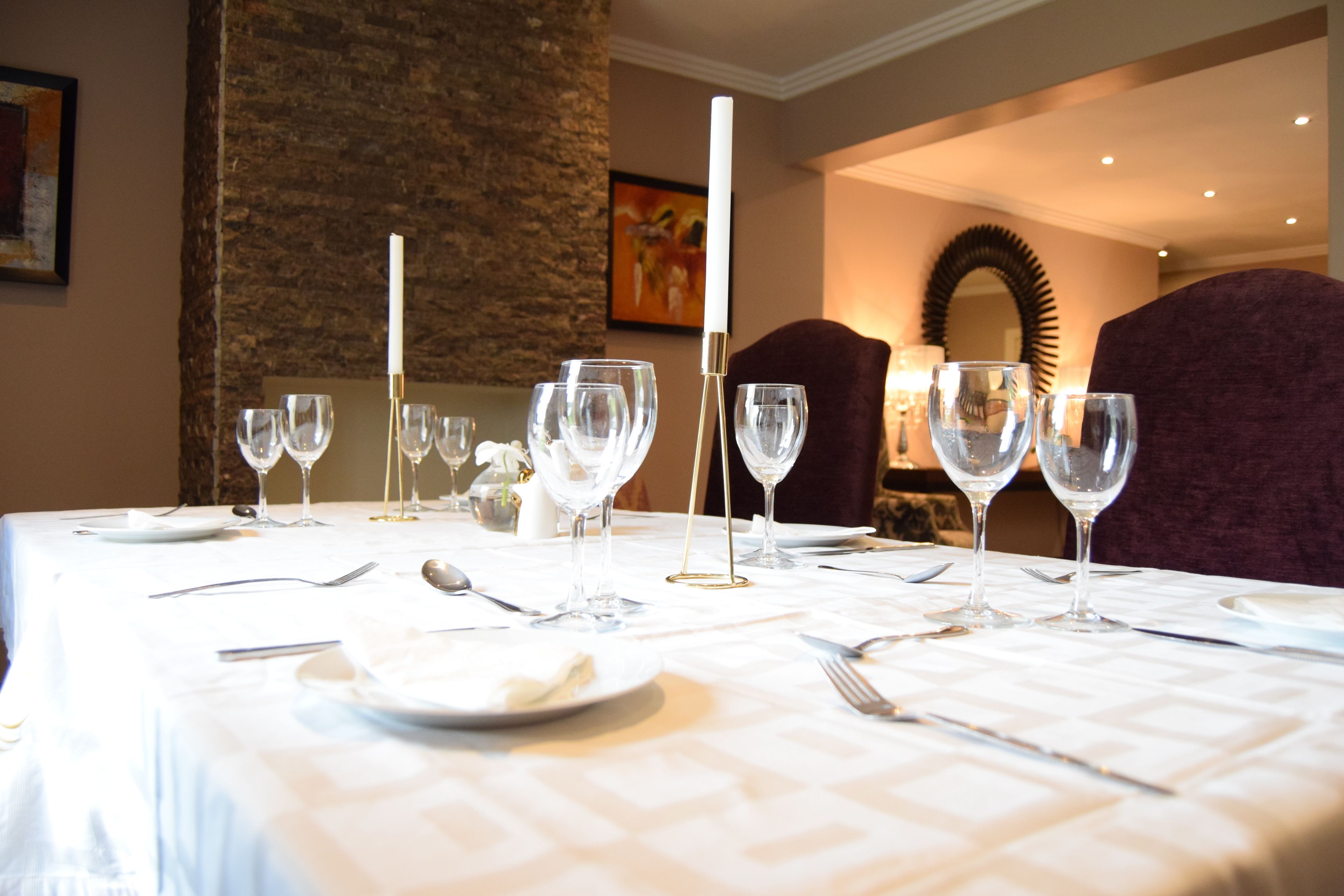 A dining table set with wine glasses, plates, and cutlery, with a candle and a mirror in the background.