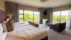Une chambre d’hôtel avec deux lits, un canapé, une télévision et de grandes fenêtres donnant sur un paysage verdoyant.