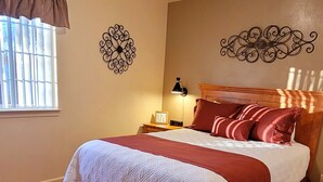 Ein Schlafzimmer mit Holzboden, einem Bett mit rotem und weißem Überwurf, einem Nachttisch mit Lampe und Wanddekoration.