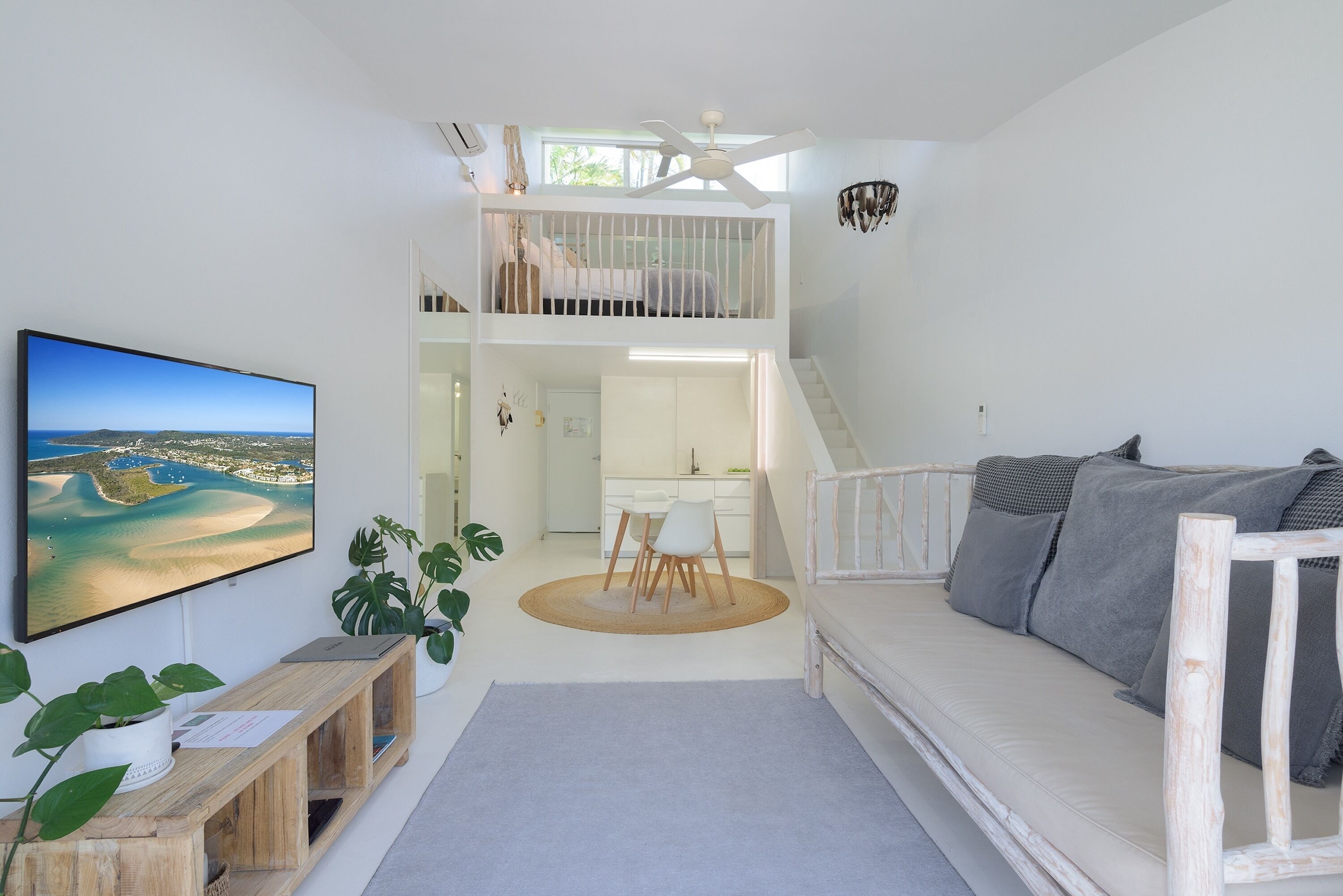 A spacious living area with a large flat-screen TV, a wooden bench, a sofa, and a staircase leading to an upper level.