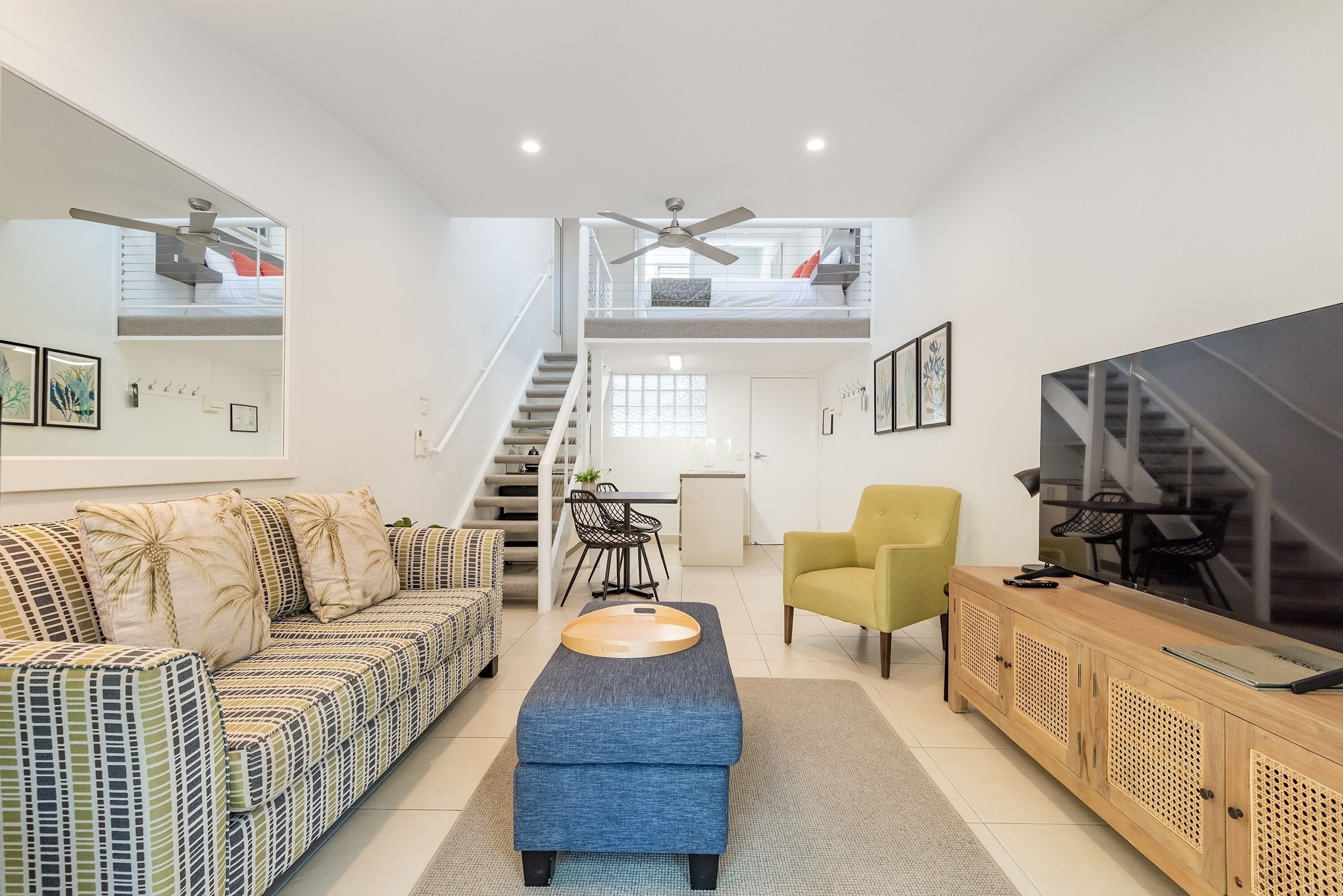 A modern living room with a sofa, ottoman, TV, and a staircase leading to a loft.