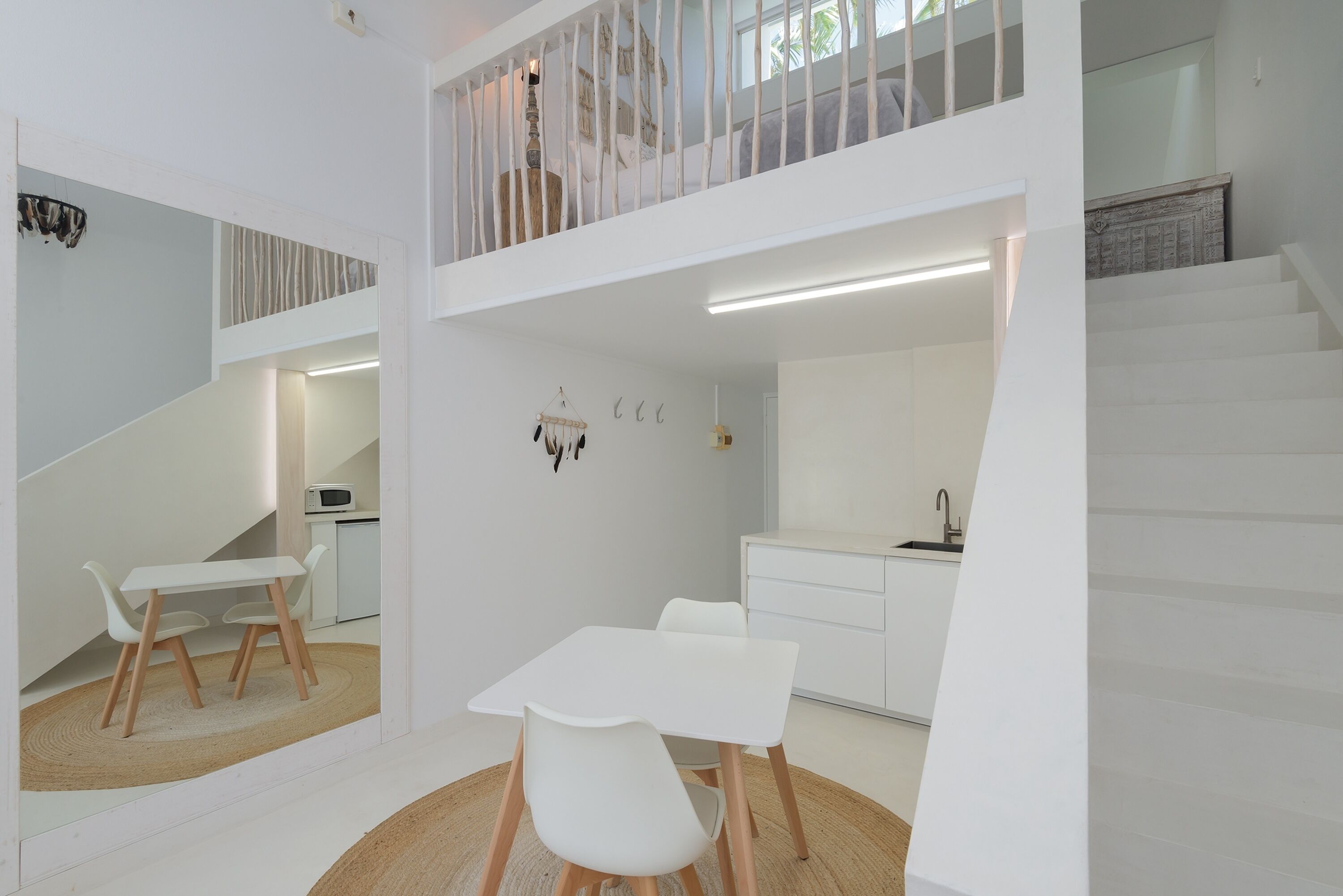 Un intérieur moderne aux tons clairs, avec un espace repas, une cuisine et un escalier.