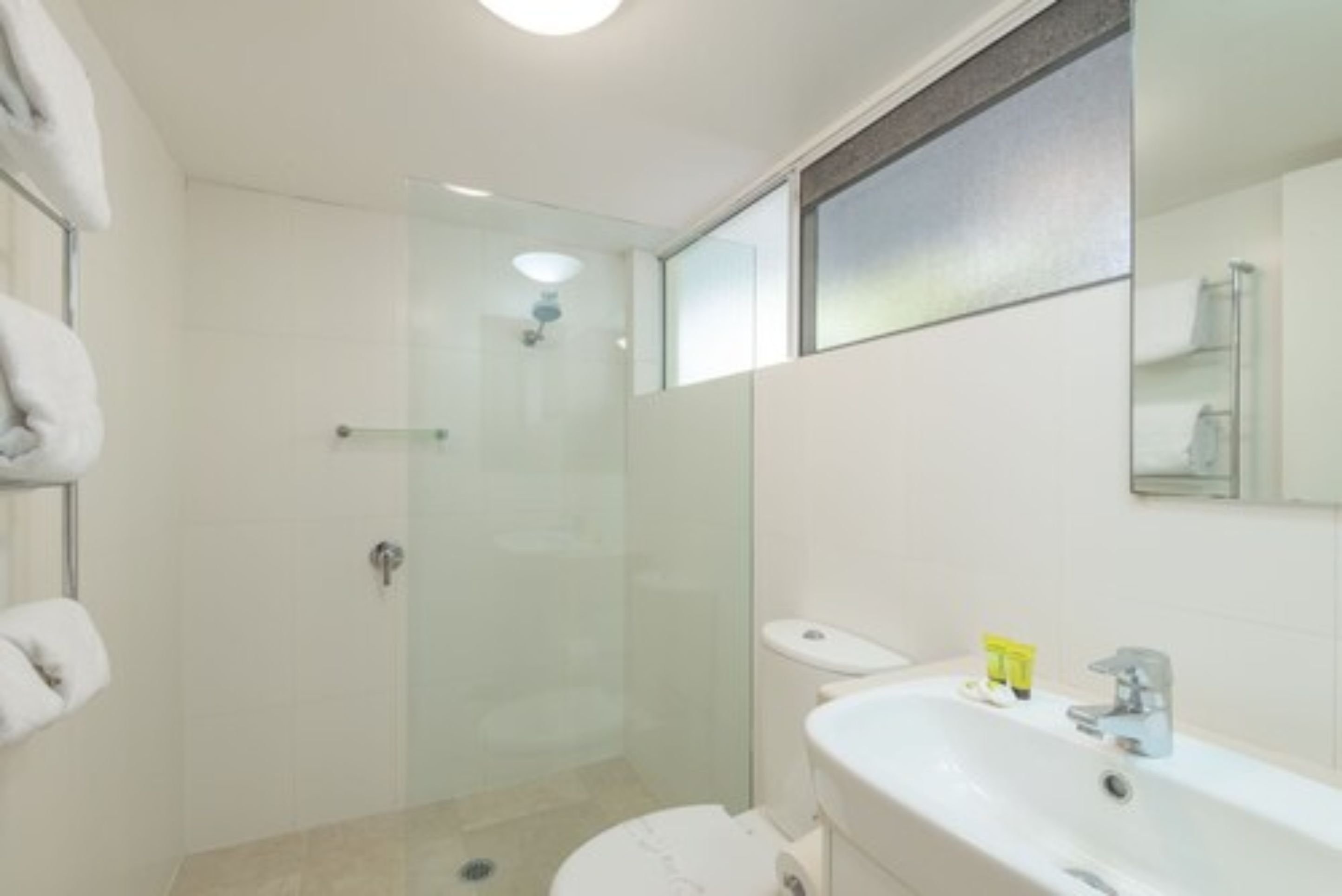 A modern bathroom with a glass-enclosed shower, a white toilet, and a sink with toiletries.
