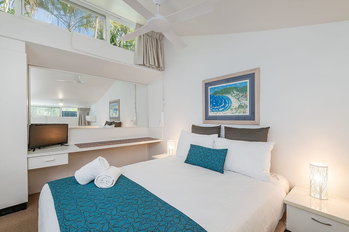A hotel room with a bed, a television, a desk, and a window with curtains.