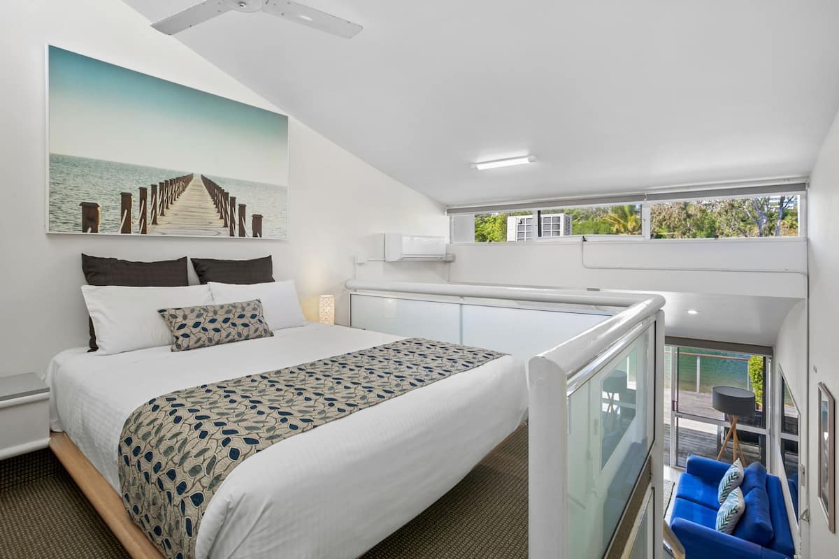 A modern hotel room with a large bed, a balcony with a view, and a painting of a pier.