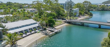 A riverside hotel with a bridge, a beach, and lush greenery.