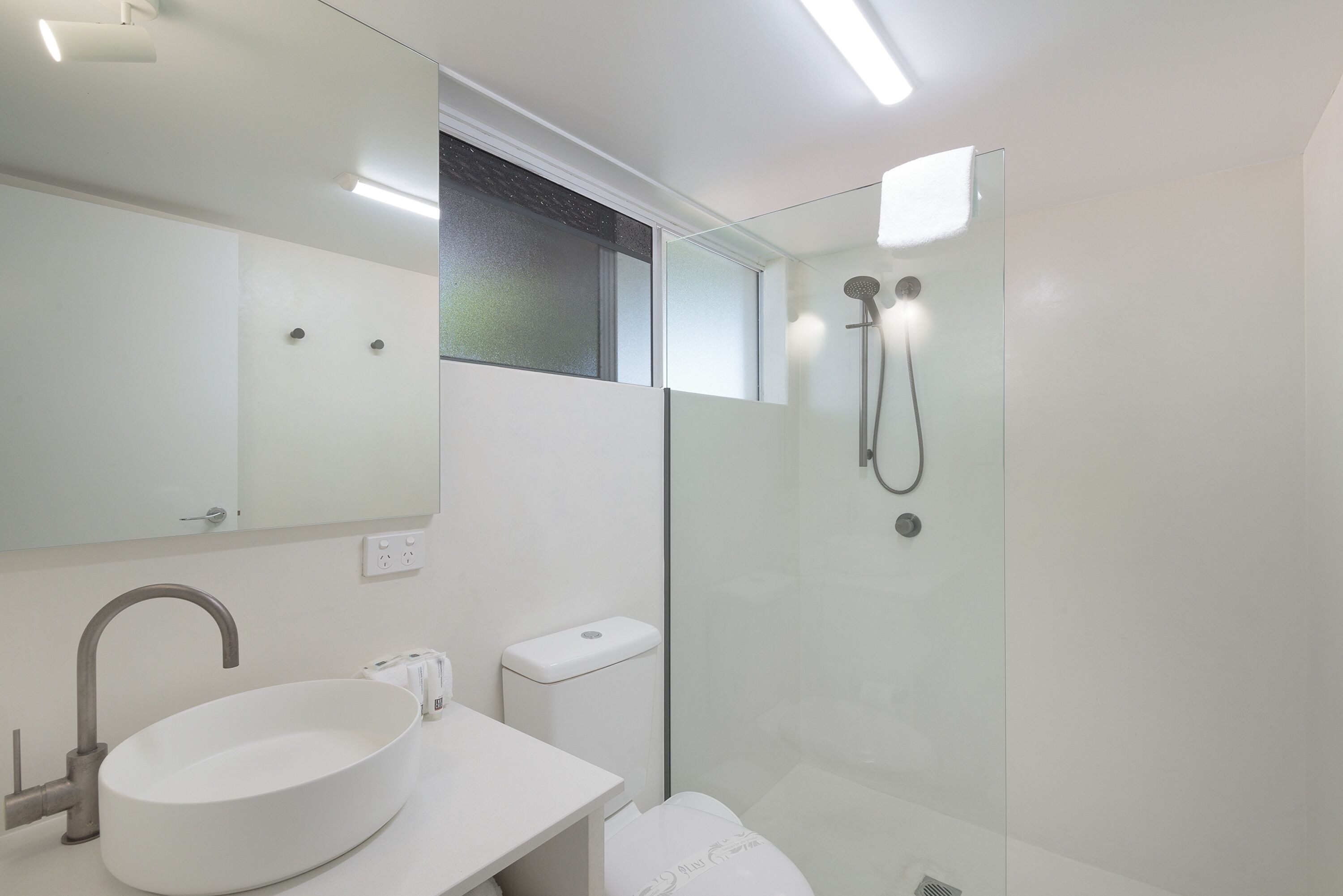 A modern bathroom with a large oval sink, a mirror, a toilet, and a glass-enclosed shower area.