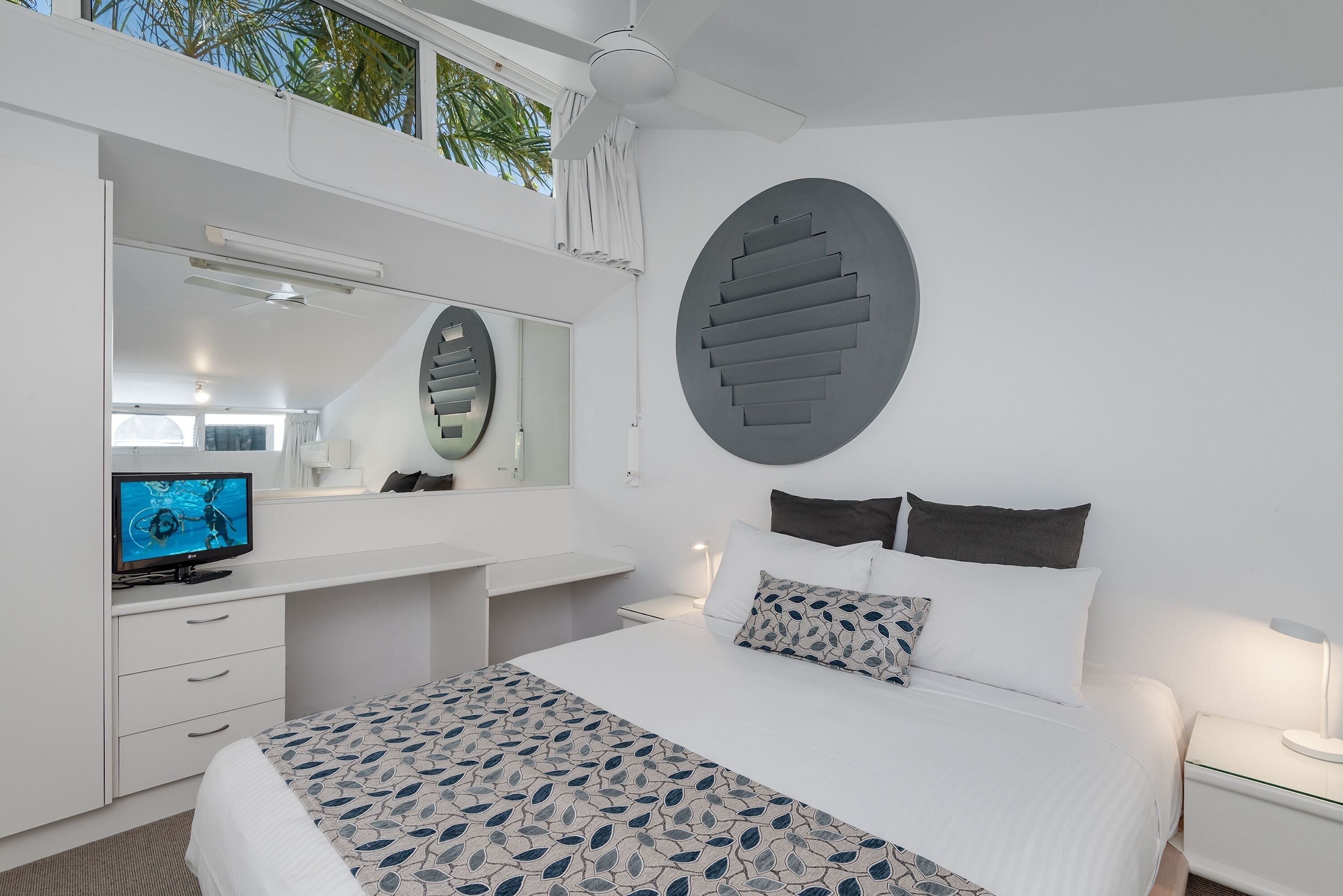 Een moderne hotelkamer met een groot bed, een televisie, een bureau en een groot raam met gordijnen.