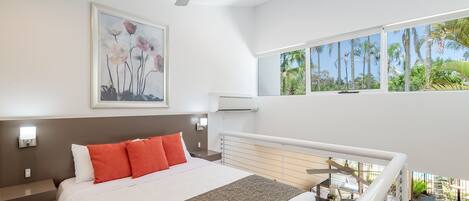 A modern hotel room with a large bed, a ceiling fan, a painting, and a view of the outdoors.