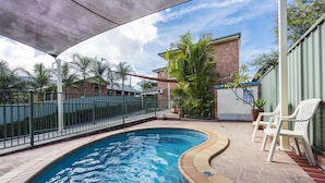 A swimming pool with a curved edge, surrounded by a brick patio and a metal fence. - Bent Street Motor Inn (South Grafton)