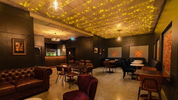A lounge area with a brown leather sofa, a red velvet chair, and multiple tables and chairs. - Bent Street Motor Inn (South Grafton)