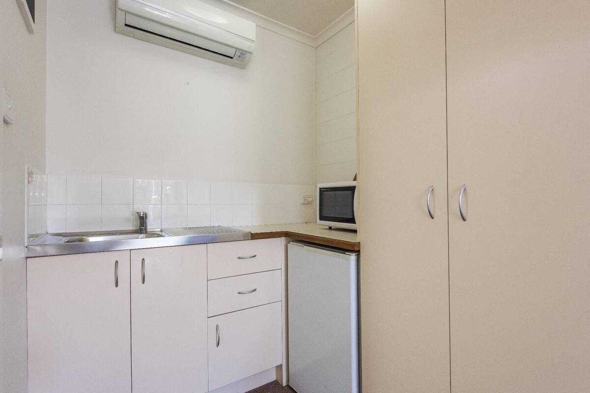 A kitchen with white cabinets, a stainless steel sink, a microwave, and an air conditioner.