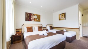 A hotel room with two beds, a wooden nightstand, and a wall-mounted artwork. - Bent Street Motor Inn (South Grafton)