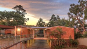 A building with a brick exterior, a covered outdoor area with a staircase, and a view of trees and sky. - Bent Street Motor Inn (South Grafton)