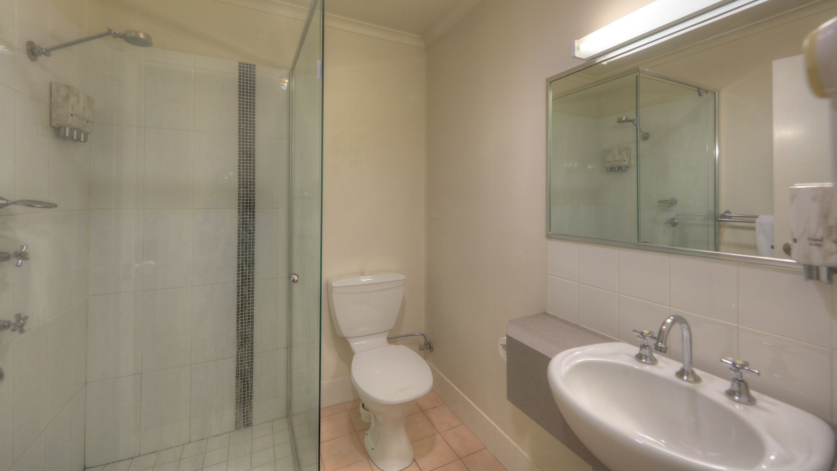 Un baño con ducha envuelta en vidrio, inodoro y lavamanos con espejo superior.