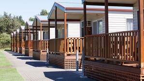 A row of wooden cabins with attached porches, each featuring a window and a door. - Gateway Lifestyle Birubi Beach (Anna Bay)