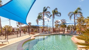 A swimming pool with a curved edge, surrounded by palm trees and lounge chairs. - Gateway Lifestyle Birubi Beach (Anna Bay)