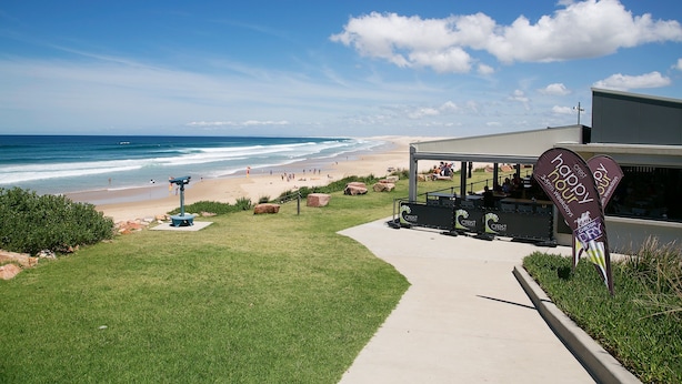 A beach view with a pathway leading to a building with a Crest logo. - Gateway Lifestyle Birubi Beach (Anna Bay)