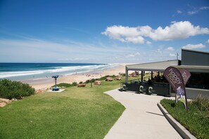 A beach view with a pathway leading to a building with a Crest logo. - Gateway Lifestyle Birubi Beach (Anna Bay)