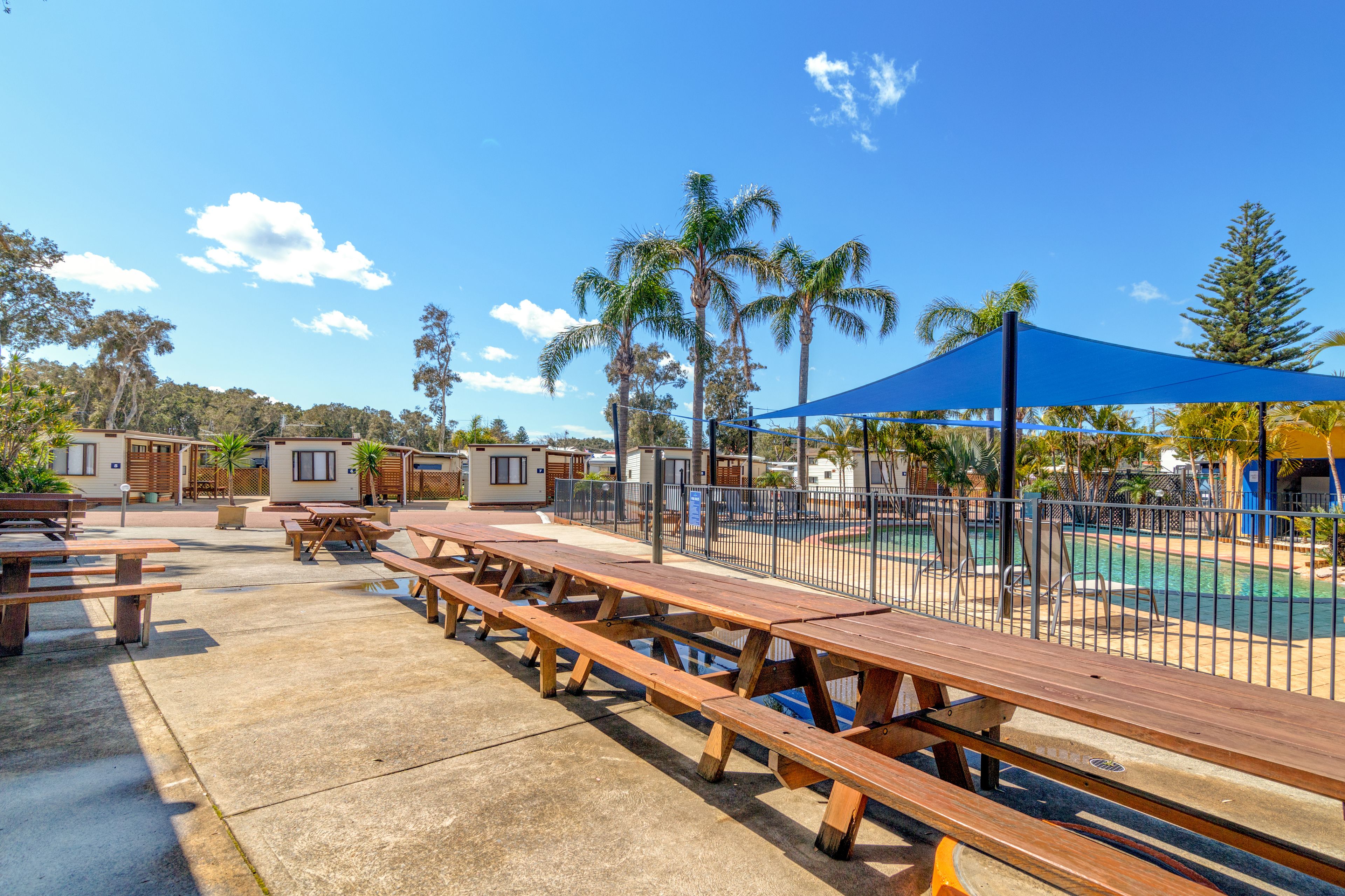 A poolside area with picnic tables, a blue canopy, and a fenced swimming pool.