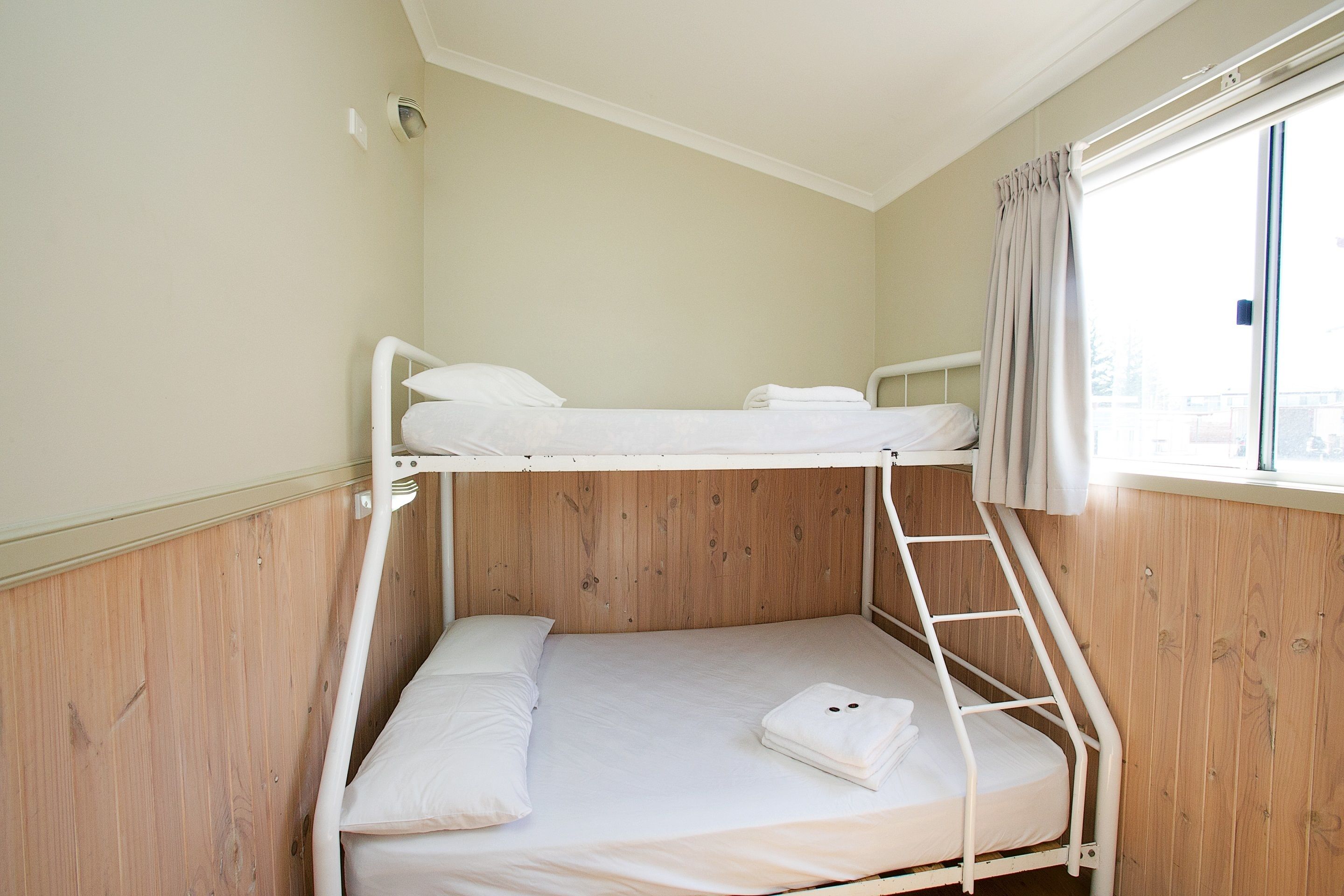 Een slaapkamer met een stapelbed, een houten wand, een raam met gordijnen en een wit plafond.