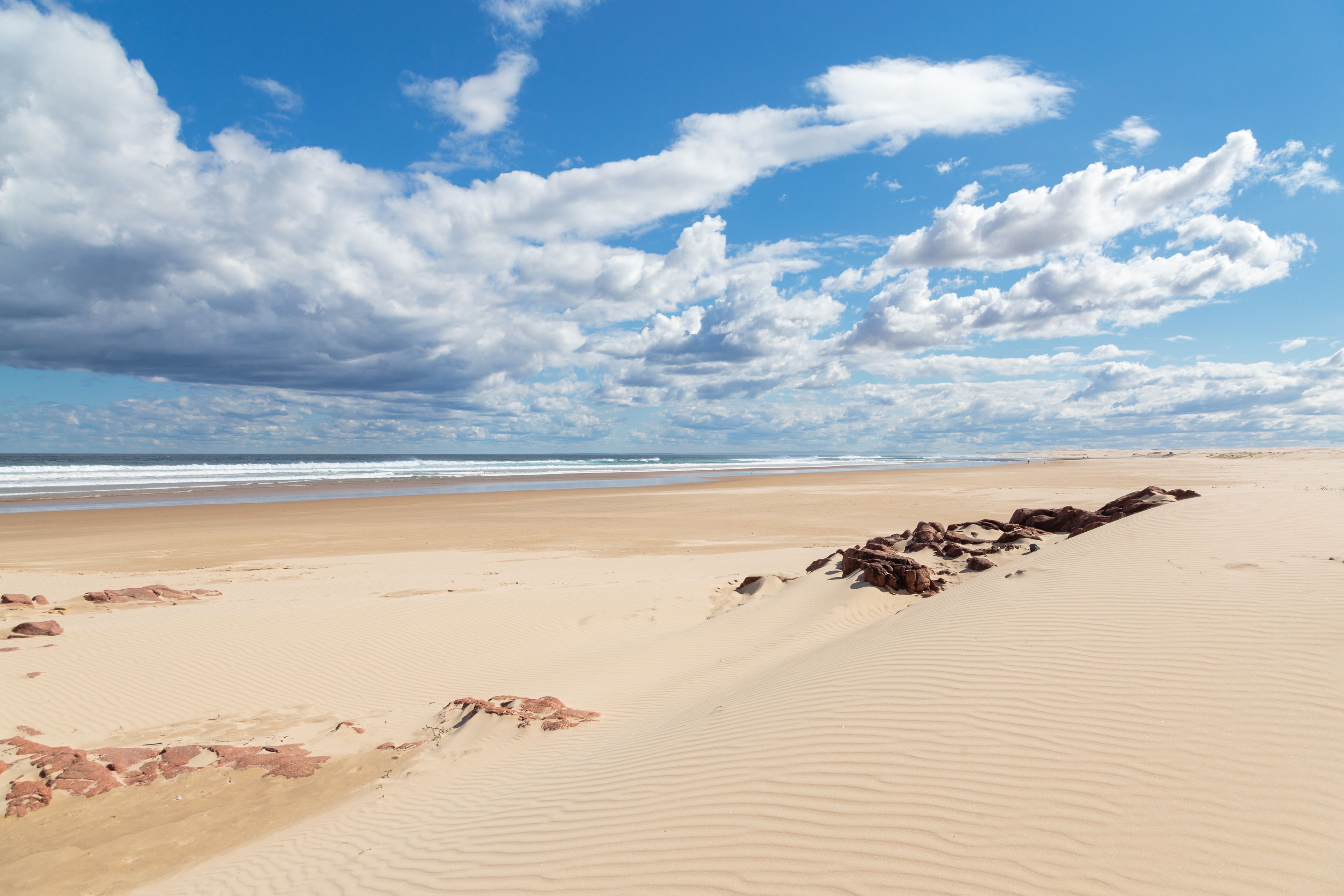 Une plage de sable fin, avec un ciel dégagé et quelques nuages épars.