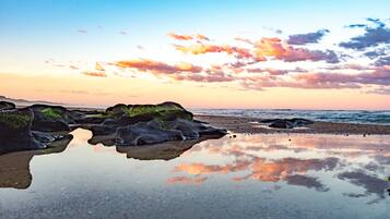 A beach with rocks and calm water reflecting the sky.