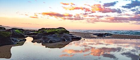 A beach with rocks and calm water reflecting the sky.