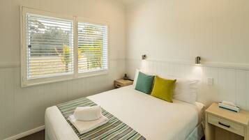 A neatly made bed with a striped bedspread, two pillows, and a bedside table with a lamp and a tissue box.