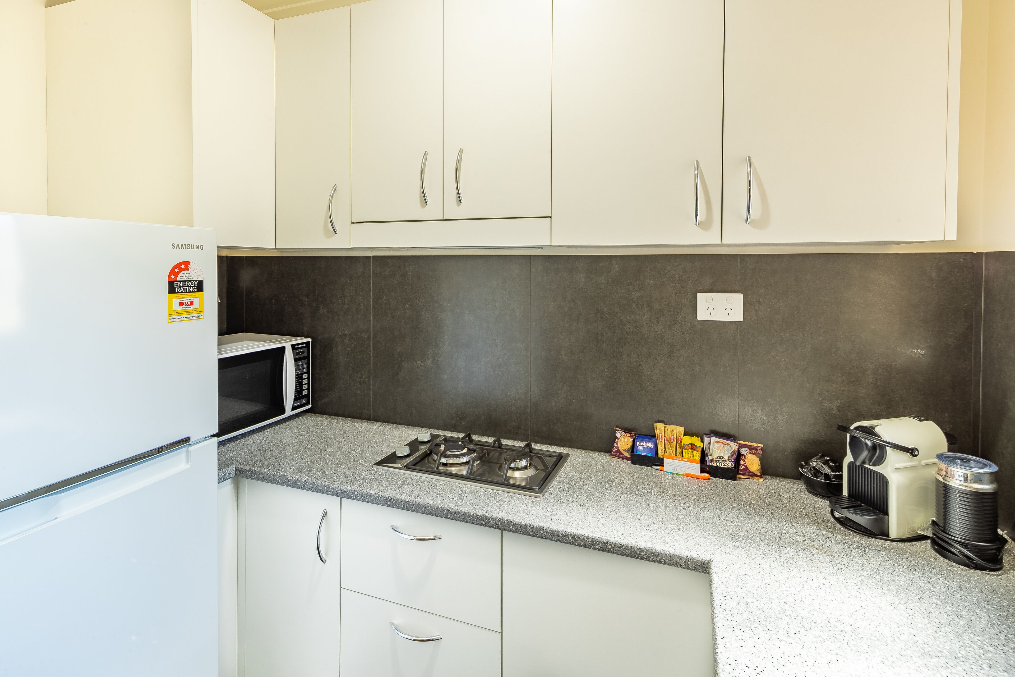 A compact kitchen with a white refrigerator, a microwave, a gas stove, and a coffee maker.