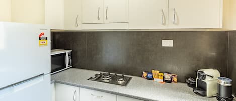 A compact kitchen with a white refrigerator, a microwave, a gas stove, and a coffee maker.