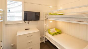 A bunk bed room with a TV mounted on the wall, a dresser, and a window with blinds.