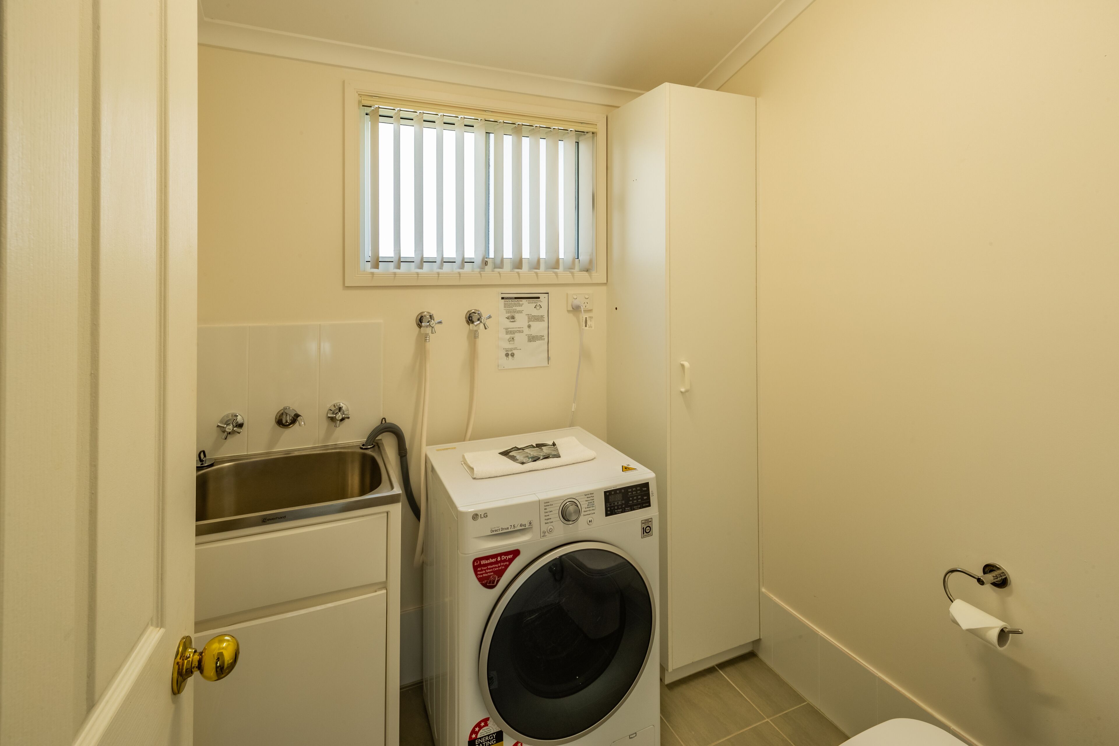 A compact laundry room with a washing machine, a sink, and a window.