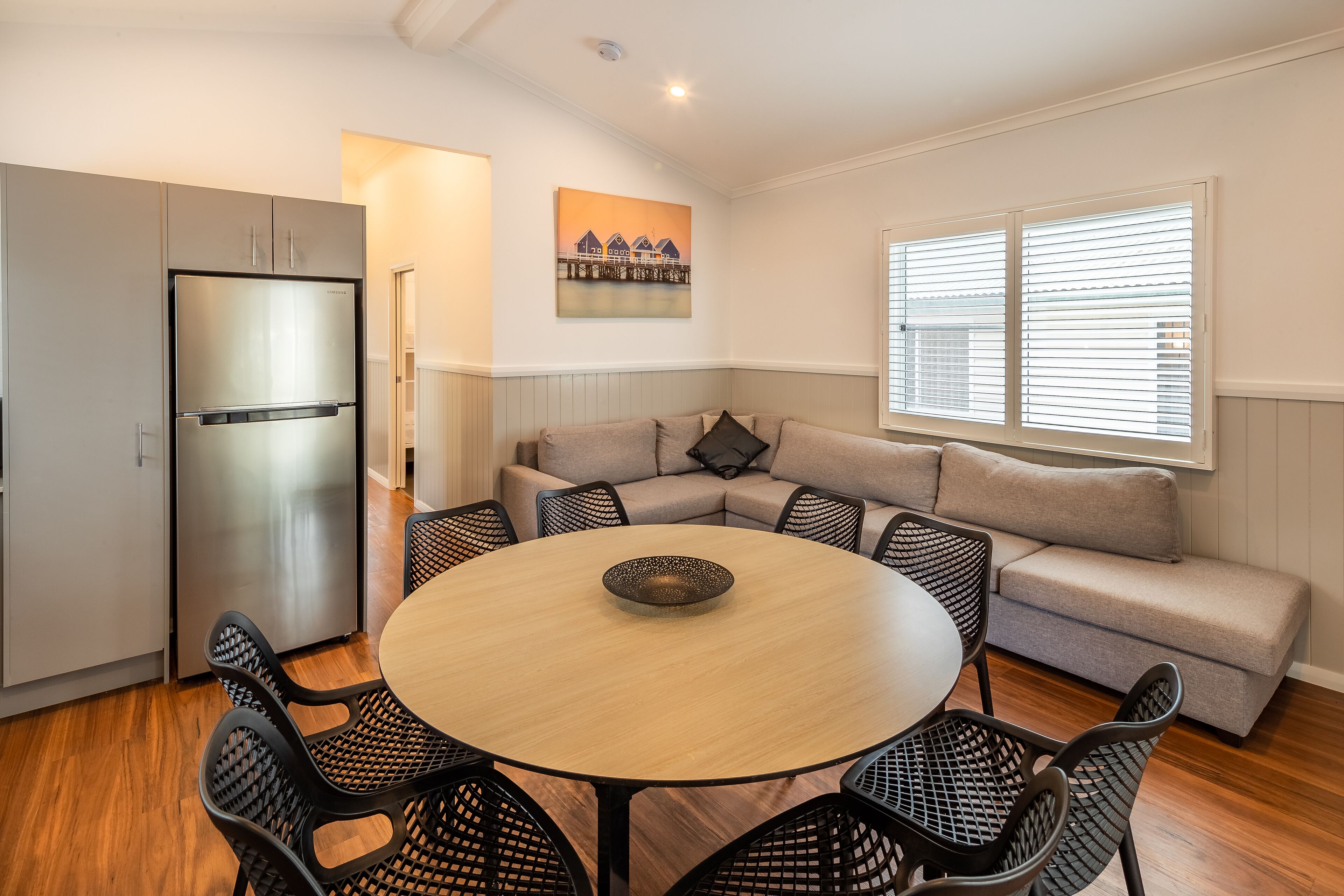 Een moderne keuken met een inbouwkoelkast, een eettafel met stoelen, een bank en een raam met jaloezieën.