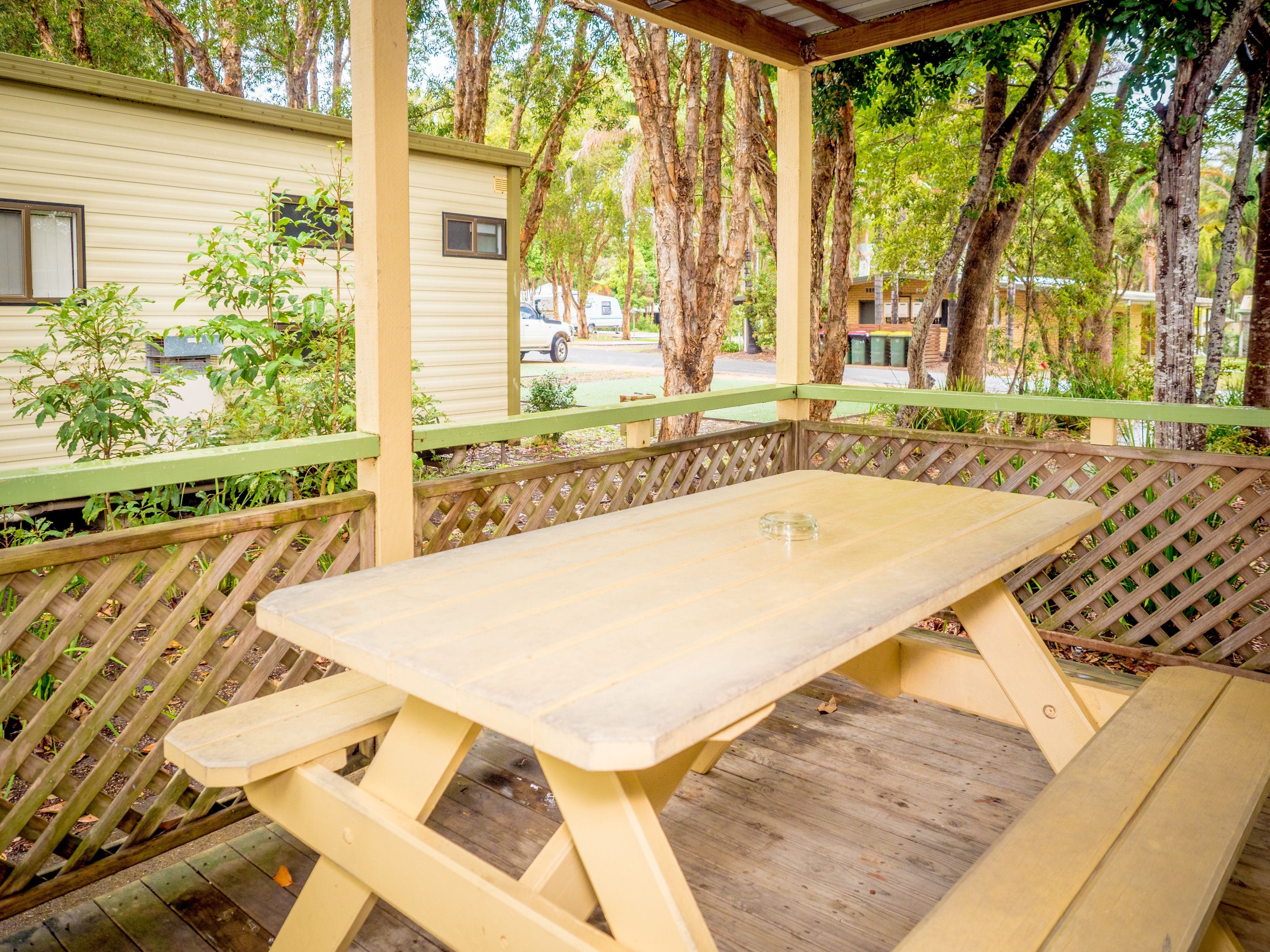 Een overdekte picknicktafel met een bank, omgeven door een houten omheining en bomen.