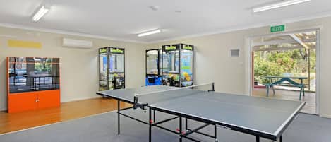 A ping pong table in a room with arcade games and an exit sign.