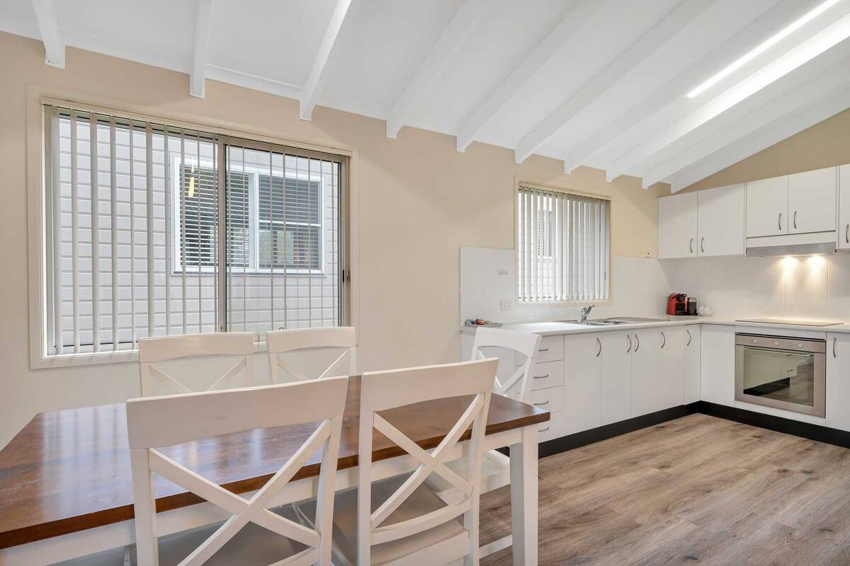 Una cocina moderna con armarios blancos, una mesa de comedor de madera y dos sillas blancas.