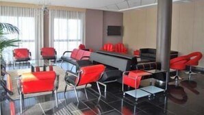A modern hotel lobby with red and black seating, a large reception desk, and a large pillar. - Cuatro Hermanas (Sagunto)
