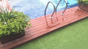 A swimming pool with metal ladders, surrounded by a wooden deck and green plants. - Cuatro Hermanas (Sagunto)