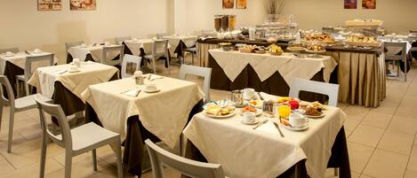 Un comedor con varias mesas dispuestas para el desayuno, que incluye un bufé con diversas opciones de comida y bebidas.