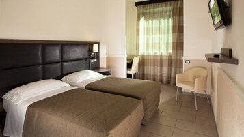 A hotel room with two beds, a desk, a chair, a TV mounted on the wall, and a window with curtains.
