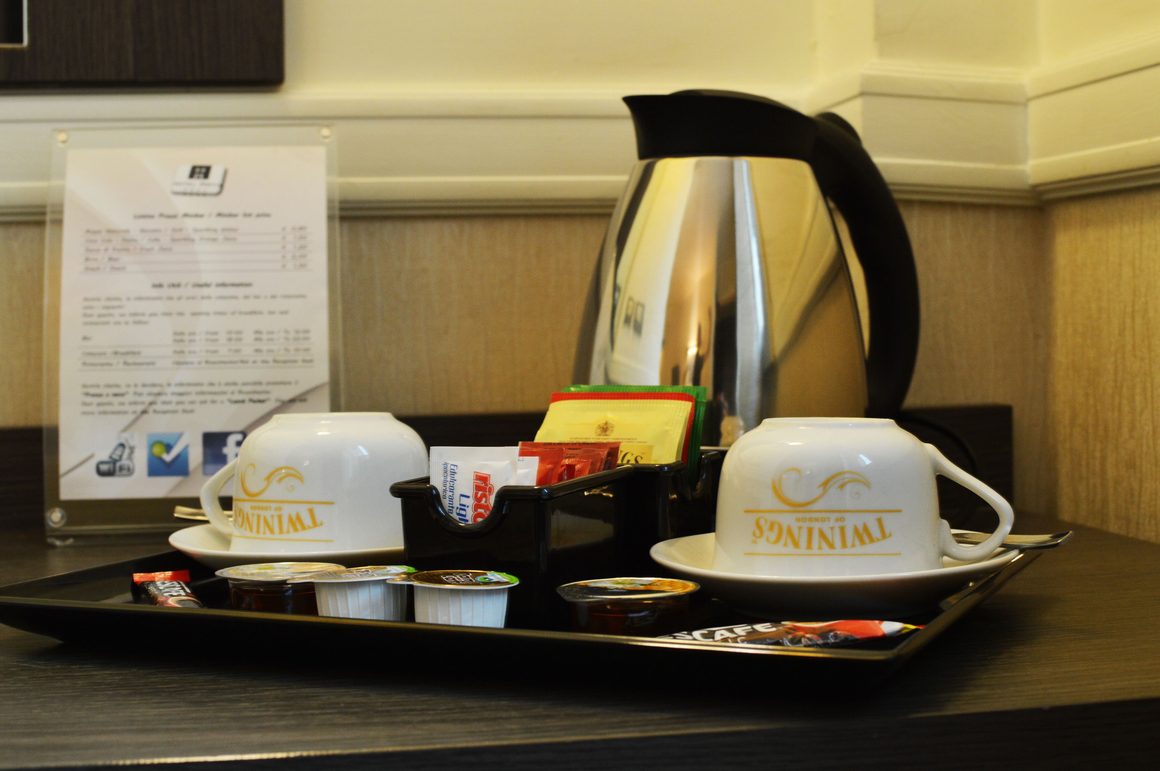 A tray with two cups labeled "TWINNIL," a coffee pot, and a menu sign in a hotel setting.