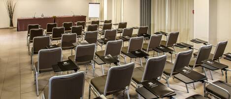 A conference room with rows of chairs and tables, a podium, and a projector screen.