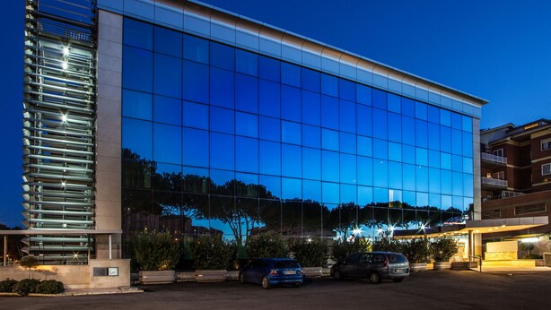 Een modern gebouw met een spiegelende glazen gevel, een parkeerplaats met auto's en een heldere lucht.