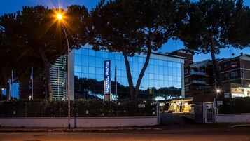 A modern hotel with a glass facade, a prominent vertical sign, and a well-lit entrance.