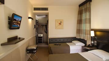 Habitación de hotel con cama, mesita de noche, lámpara, televisor y una pequeña zona de estar con una maleta.