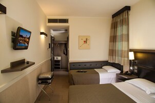 Una camera d'albergo con un letto, comodino, lampada, televisione e un piccolo angolo relax con una valigia.