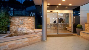 Een moderne hotelentree met een gevel van natuursteen, een receptiebalie en een glazen deur die naar binnen leidt.