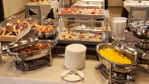 Een buffet met diverse gerechten, waaronder vleeswaren, kazen en fruit, en een stapel witte borden met vorken.